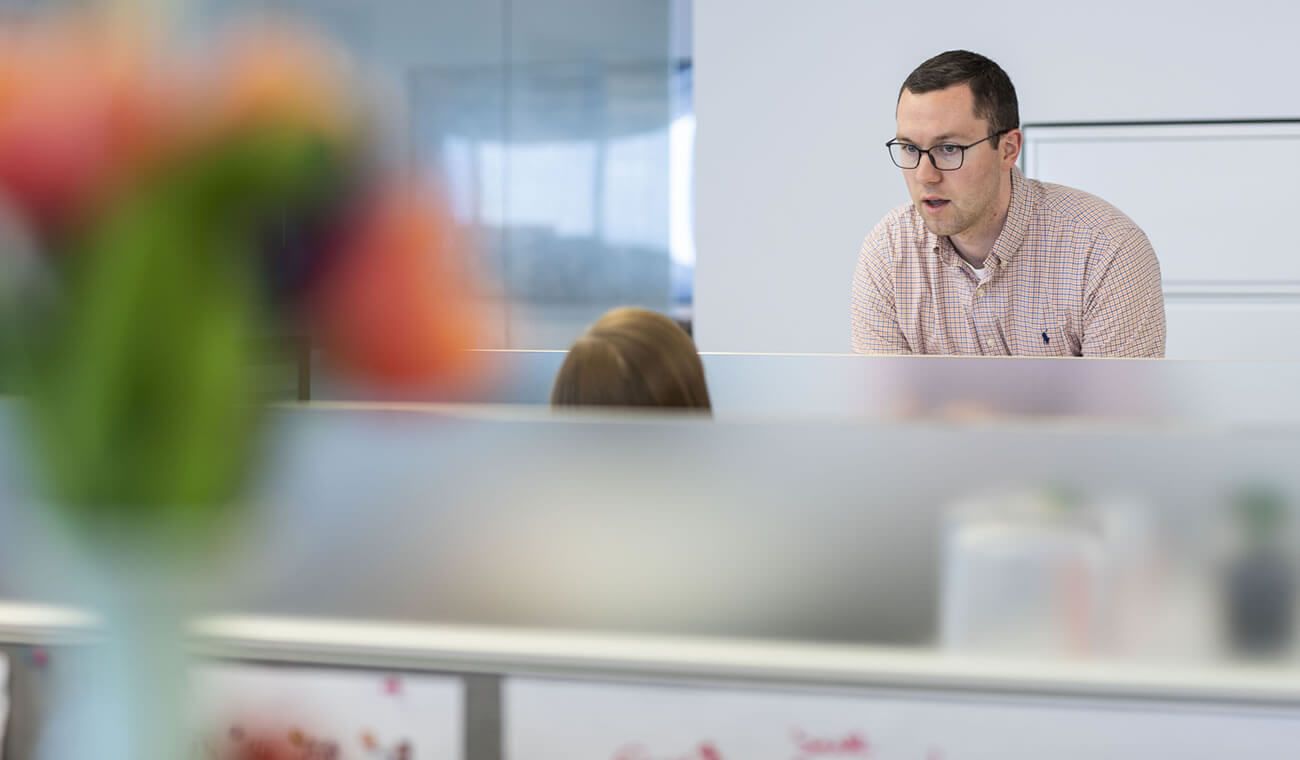 Man standing at a workstation talking to someone sitting down